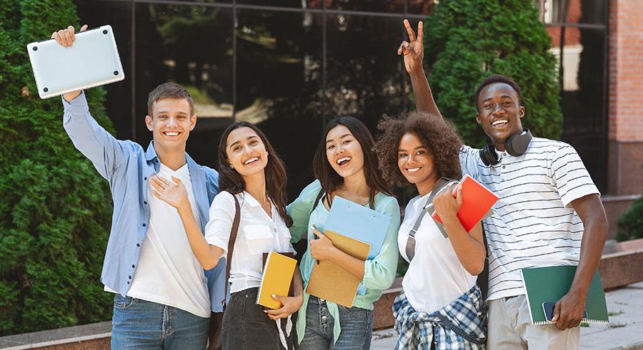 Image of happy students holding books and laptops looking at the camera smiling